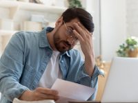 Upset frustrated young man reading bad news in postal mail letter paper document sit at home table, depressed stressed guy worried about high bill tax invoice, overdue debt notification money problem
