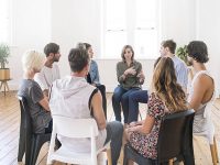 Support group gathering for a meeting. Young woman discussing with people at entrance hall. Males and females are sharing ideas during group therapy.