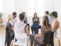 Support group gathering for a meeting. Young woman discussing with people at entrance hall. Males and females are sharing ideas during group therapy.