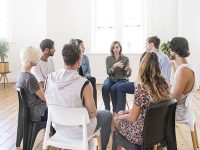 Support group gathering for a meeting. Young woman discussing with people at entrance hall. Males and females are sharing ideas during group therapy.