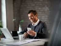 Happy entrepreneur working on a computer and using smart phone at office desk.